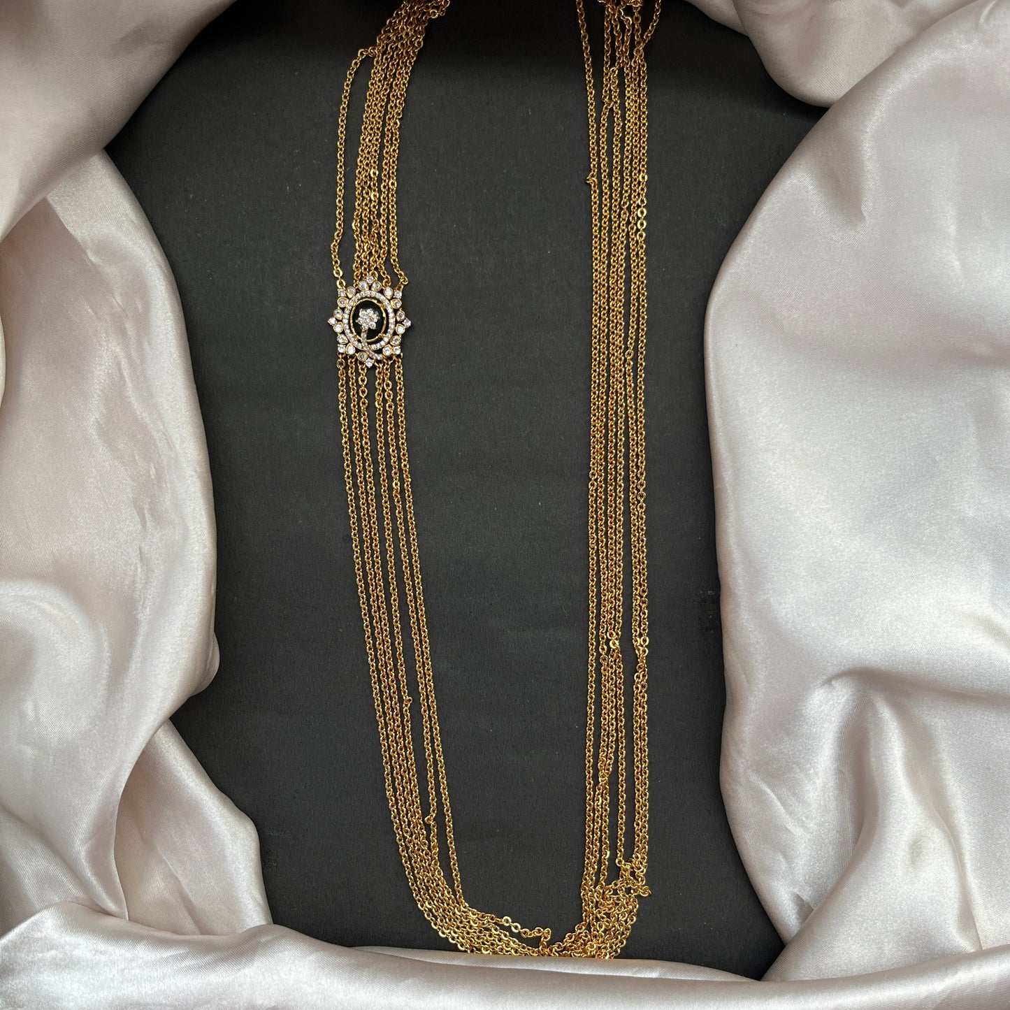 Gold necklace with a decorative clasp on a black cushion with white fabric