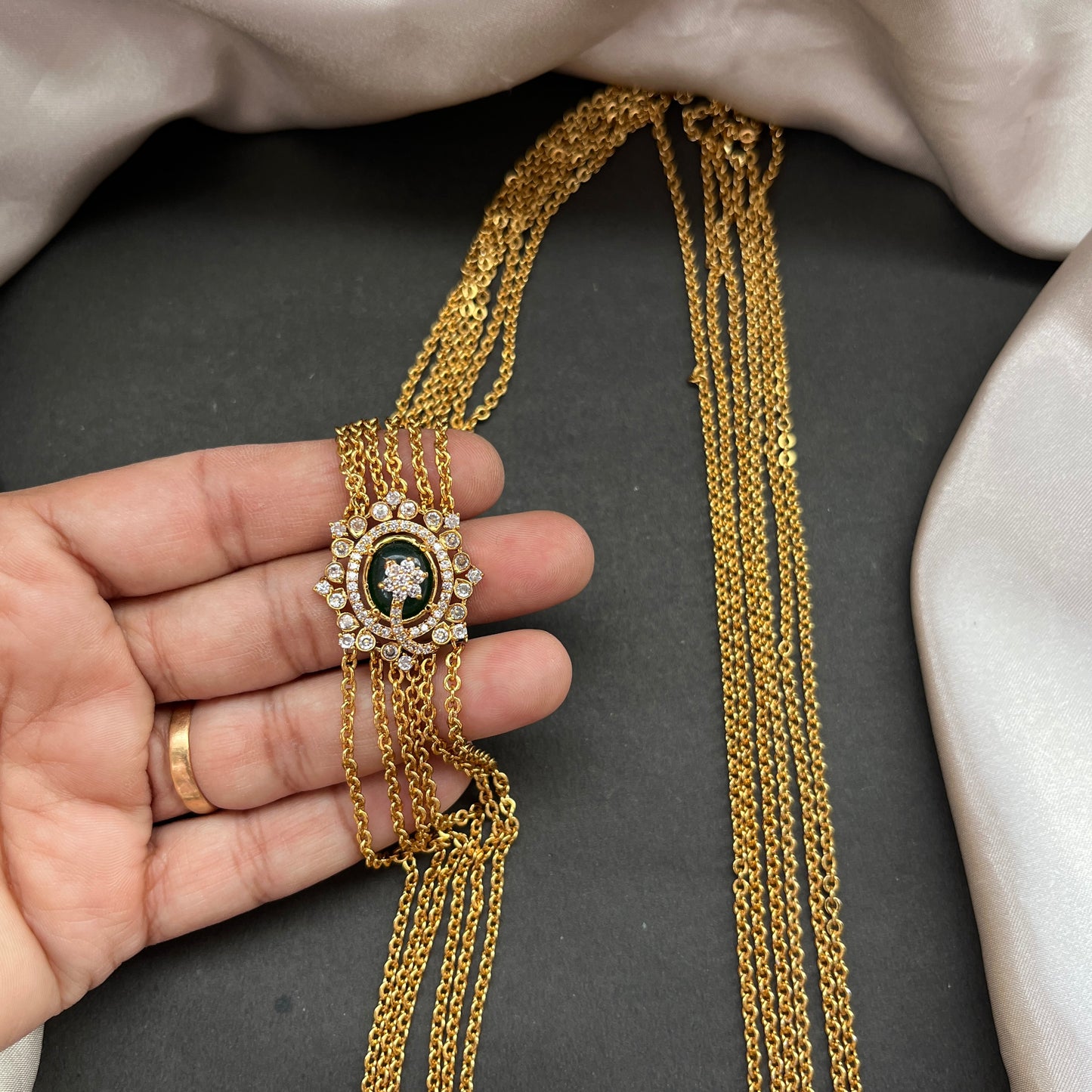 Gold necklace with a decorative clasp held by a hand on a dark surface
