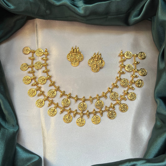 Gold necklace and earrings on a white cushion with green satin fabric