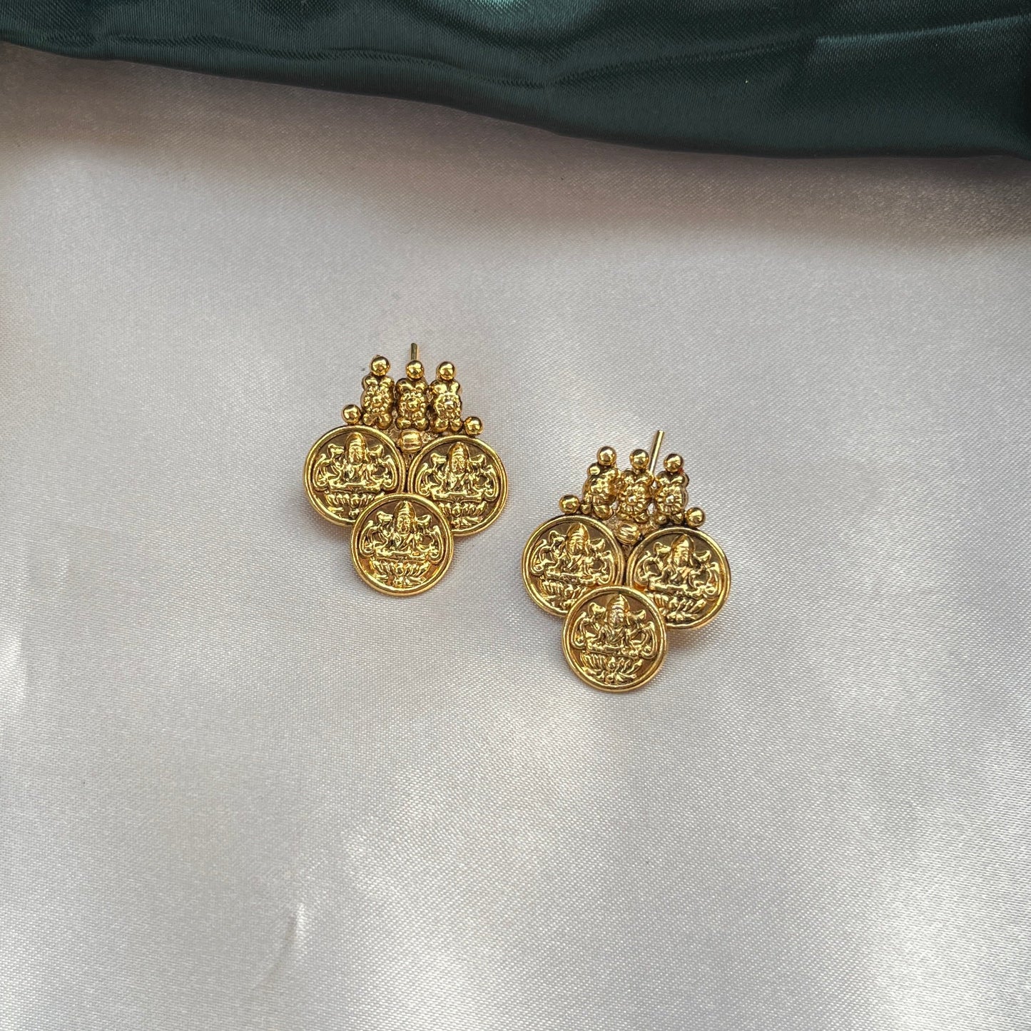 Gold earrings on a green satin surface